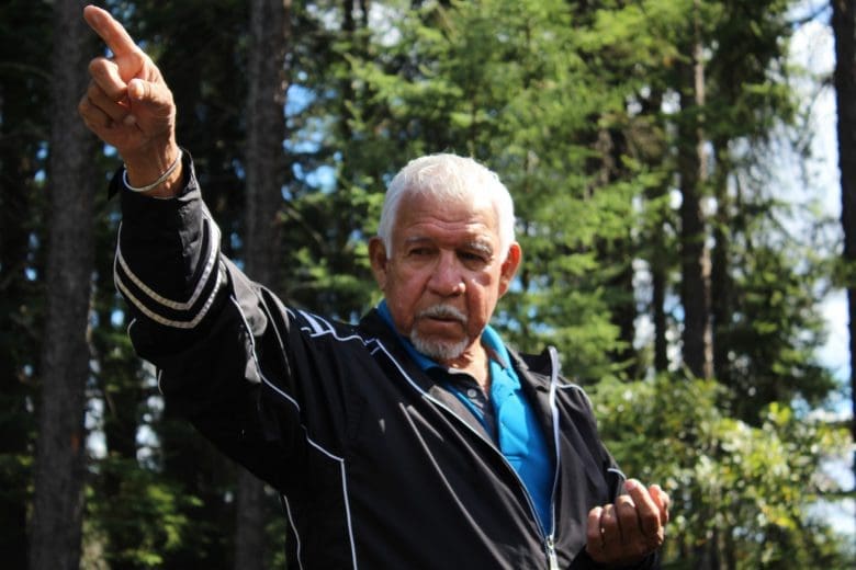 First Nations man holds hid arm up in a forest