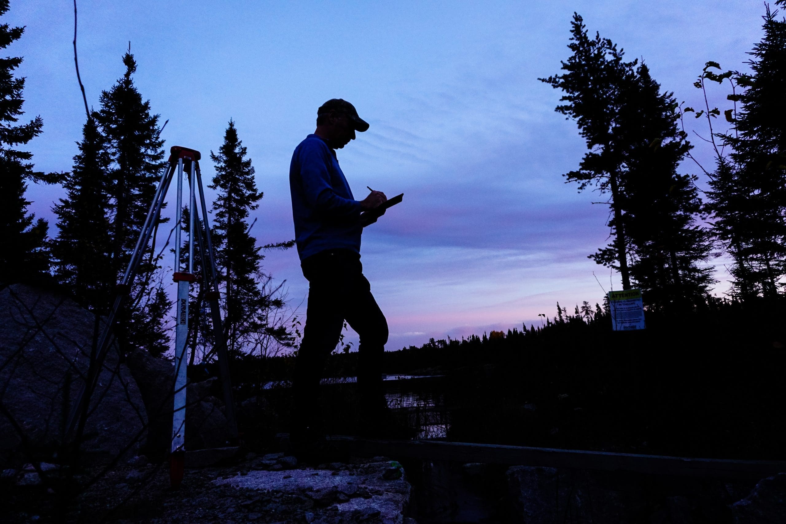 Silhouette of a man standing beside a lake taking notes