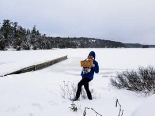 Woman standing on a frozen lake in northern Ontario, holding a sign that says '223'