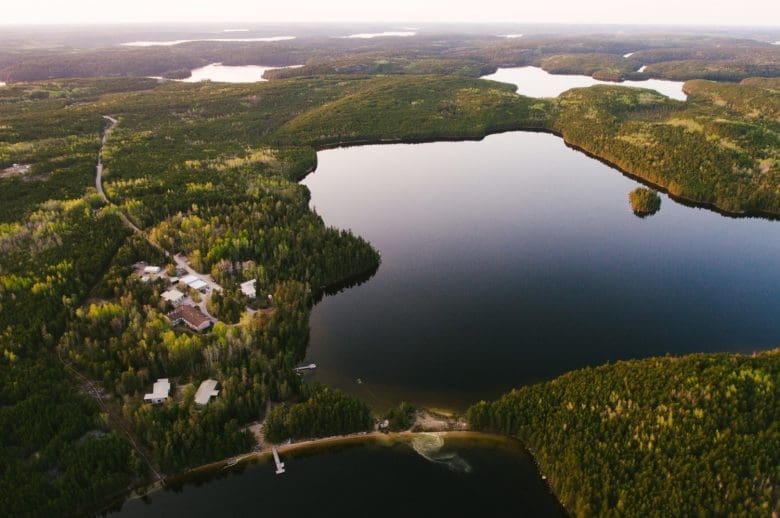 Aerial shot of a blue and silver freshwater lake surrounded by green trees and a few white buldings