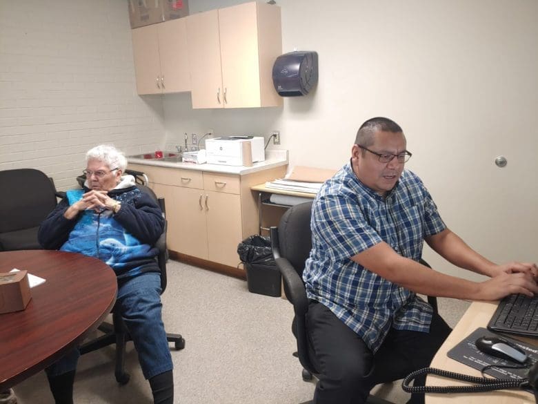 Two people sit at desks in from of computers in a room