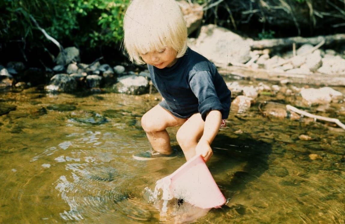 A child holds a bag in a lake in the 1970s