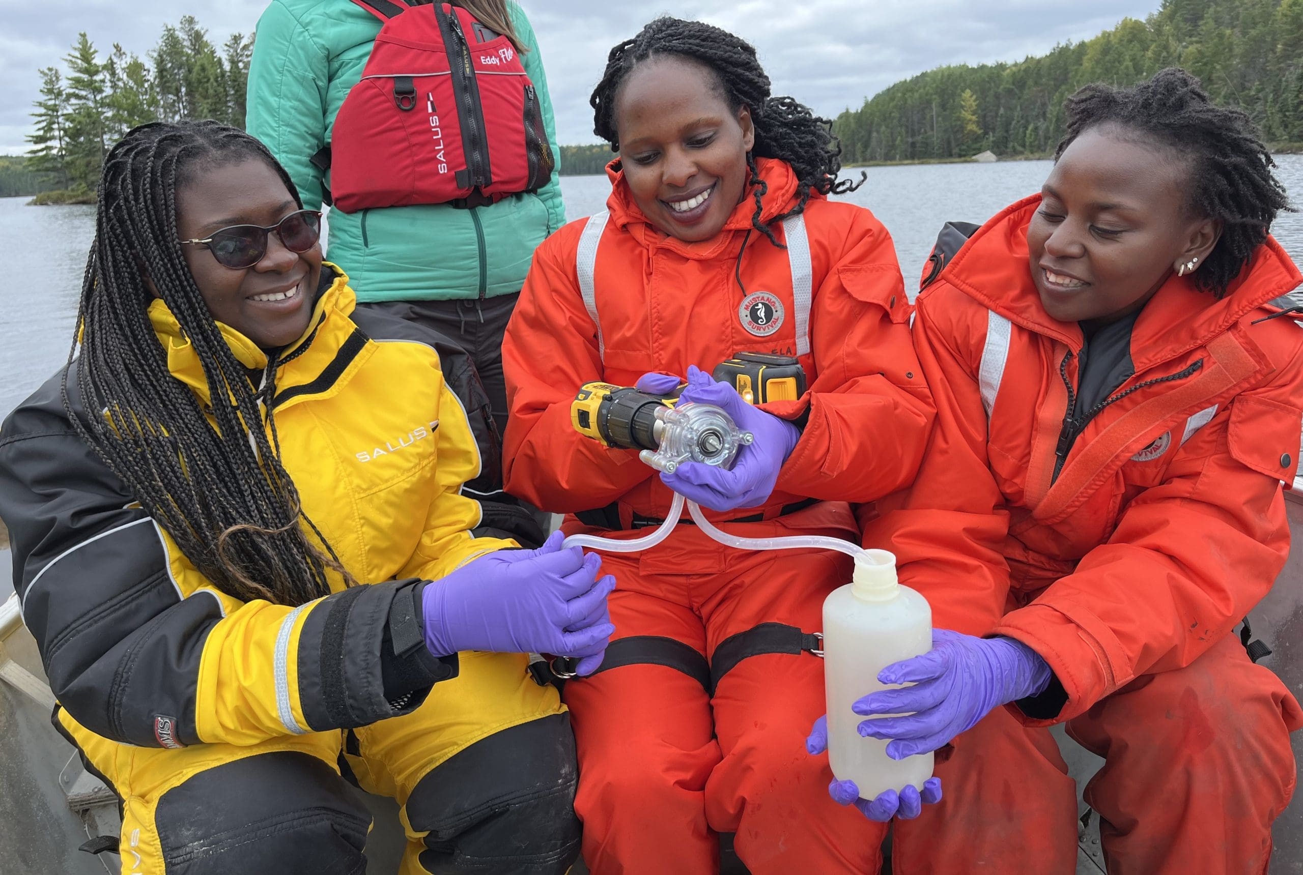 Three women in boat in lifejackets handling scientific equipment
