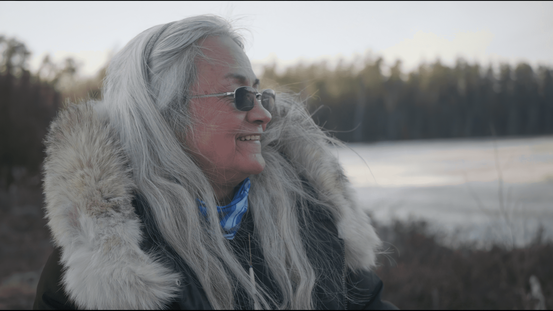 Woman with grey hair looks to the side and smiles in front of trees and lakes in Canada