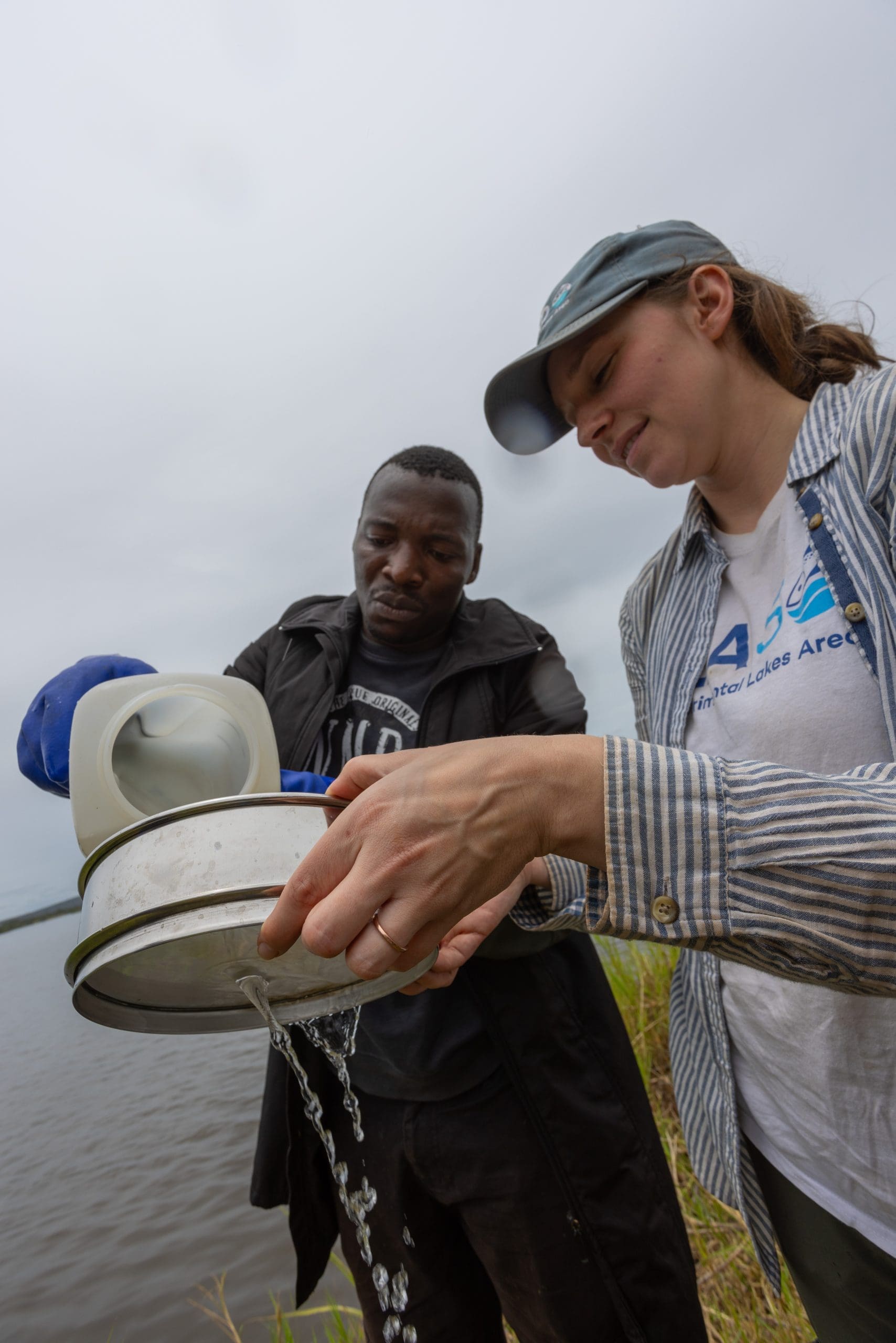 Desiree Langenfeld and Simon Muhayimana team up to filter lake water through a sieve to collect microplastics for counting back at the lab.